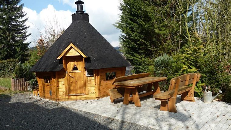 Eine gemütliche Holzhütte mit einem runden Dach und einer Fassade aus Holz. Draußen stehen eine Tischgruppe und einige Bäume in der Nähe.