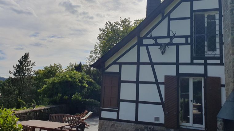 Ein charmantes Fachwerkhaus mit Holzfenstern. Draußen steht eine gemütliche Terrasse mit Gartenmöbeln und Blick auf die Natur.