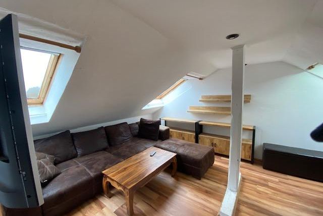 Ein moderner Dachzimmer mit einer bequemen Couch und einem Holz Tisch. Große Fenster sorgen für viel Tageslicht.