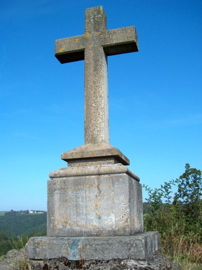 Steinkreuz auf einem Sockel vor blauem Himmel.