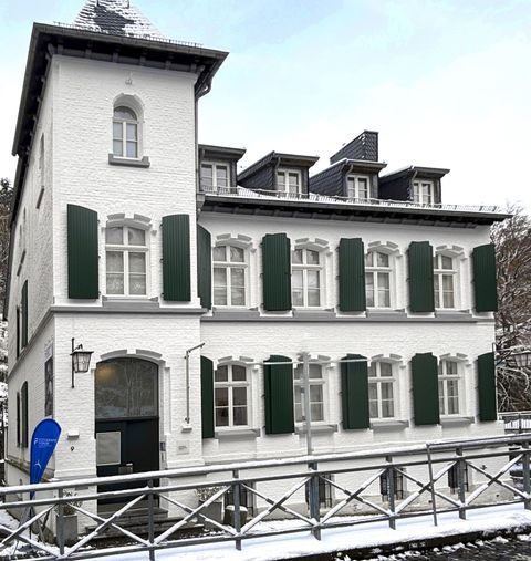 Ein elegantes weißes Gebäude mit grünen Fensterläden. Es steht in einer verschneiten Umgebung und hat ein traditionelles Design.