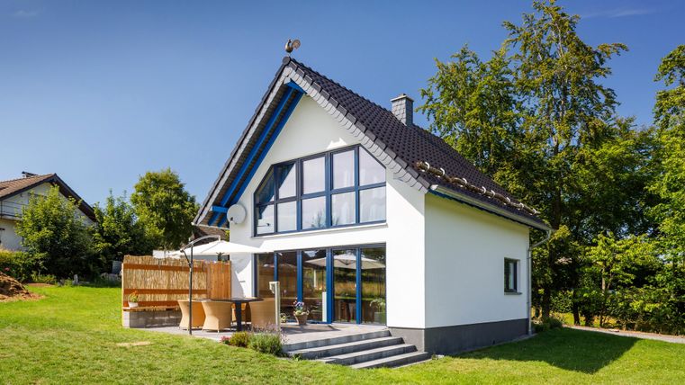 Ein modernes Haus mit großen Fenstern und einem Garten. Die Umgebung ist grün und sonnig.