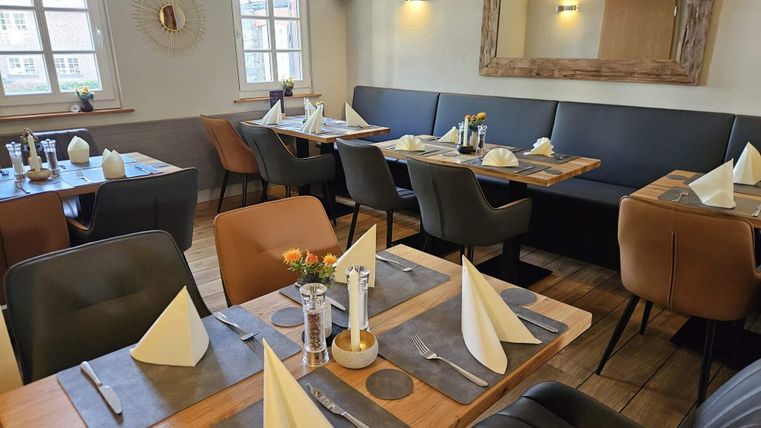 Ein gemütliches Restaurant mit eleganten Tischen und Stühlen. Die Tische sind liebevoll gedeckt und schaffen eine einladende Atmosphäre.