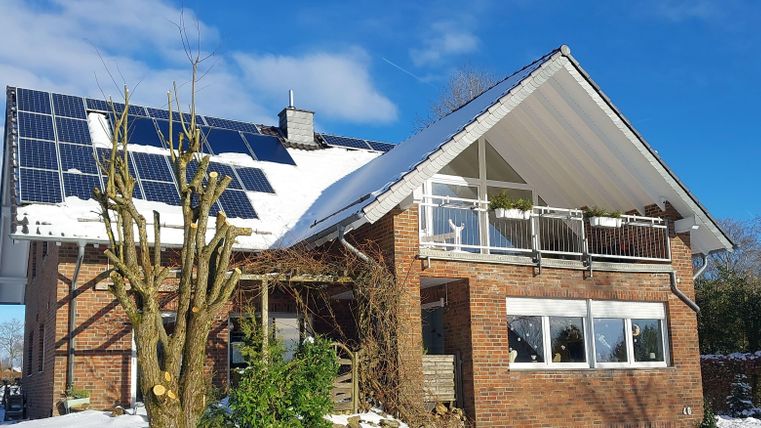 Ein modernes Haus mit Solarpanels auf dem Dach. Es liegt in einer verschneiten Umgebung unter einem klaren blauen Himmel.