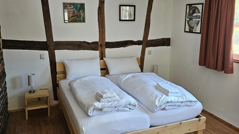 Ein gemütliches Schlafzimmer mit einem Doppelbett und hellen Bettwäsche. Die Wände sind mit Holzleisten dekoriert und es gibt einige Bilder sowie ein Fenster mit einem Vorhang.