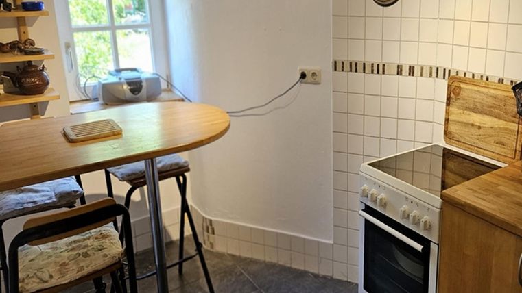 Eine kleine, moderne Küche mit einem Esstisch und Stühlen. Der Raum hat weiß geflieste Wände und eine Kochstelle.