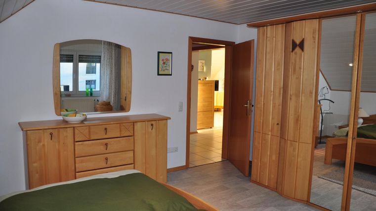 Ein gemütliches Schlafzimmer mit Holzfußboden und modernen Möbeln. Der Raum enthält einen Spiegel und einen großen Kleiderschrank.