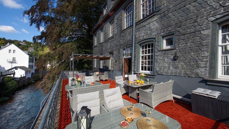 Eine gemütliche Terrasse mit stilvollen Möbeln und Blick auf einen Fluss. Ideal zum Entspannen an einem sonnigen Tag.