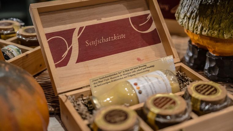 Eine Holzbox mit verschiedenen Senfsorten und einem speziellen Senf. Die Verpackung ist ansprechend gestaltet und zeigt das Produkt in einer eleganten Präsentation.