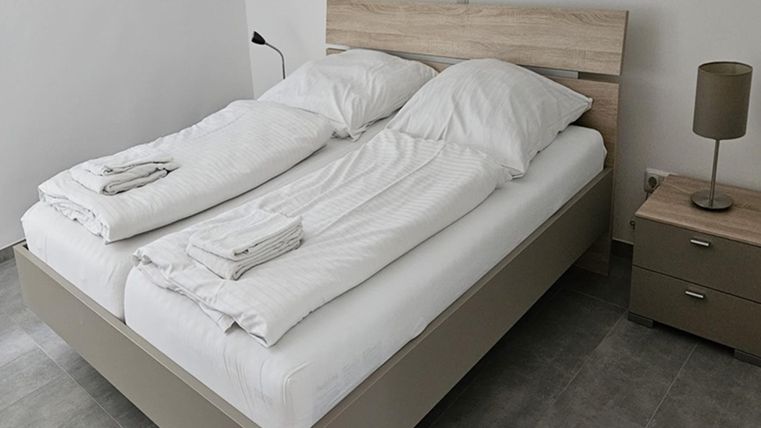 Ein modernes Schlafzimmer mit einem Doppelbett und frischen Bettwäsche. Neben dem Bett steht ein Nachttisch mit einer Lampe.