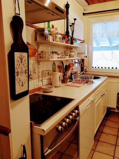 Eine gemütliche Küche mit weißen Schränken und einem Herd. Auf den Regalen stehen verschiedene Kochutensilien und Gewürze.