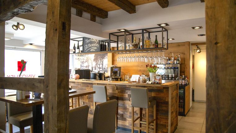 Eine gemütliche Bar mit einem Holztheke und modernen Stühlen. Die Einrichtung kombiniert rustikalen Charme mit einer einladenden Atmosphäre.