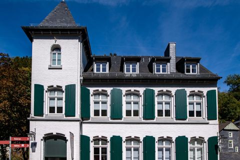 Ein historisches Gebäude mit weißen Wänden und grünen Fensterläden. Der Himmel ist klar und blau.