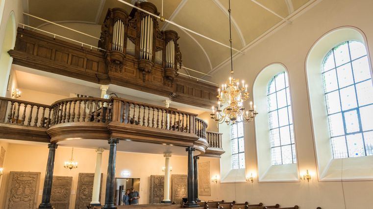 Eine Innenansicht einer Kirche mit einer Orgel auf der Empore. Die Wände sind hell und große Fenster lassen viel Licht herein.