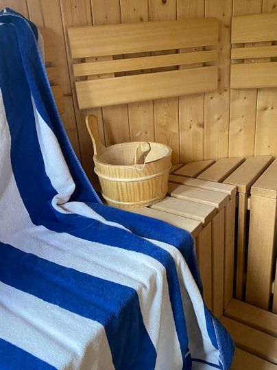 Eine gemütliche Sauna mit Holzbank und einem Auswahl handgewebter Handtücher. Im Raum steht ein Holzeimer, der auf der Bank platziert ist.