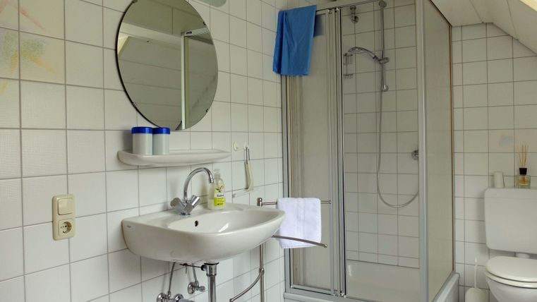 Ein helles Badezimmer mit weißen Fliesen. Es verfügt über ein Waschbecken, eine Dusche und eine Toilette.