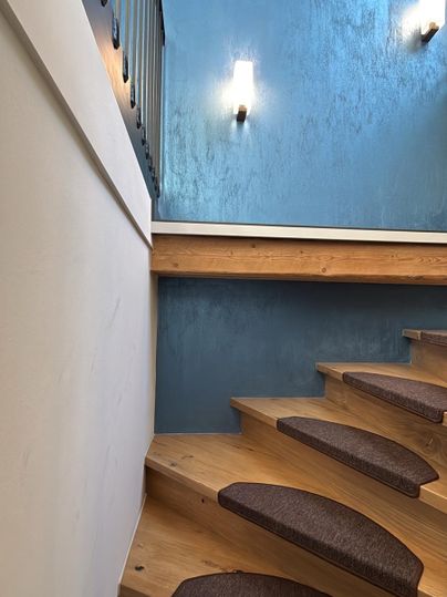 Eine moderne Treppe aus Holz mit gepolsterten Stufen. Die Wände sind in einem stilvollen Blau gestrichen und die Beleuchtung sorgt für eine angenehme Atmosphäre.