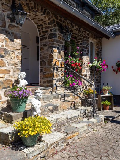 Ein schöner Eingangsbereich mit Steinmauer und bunten Blumenpflanzen. Die Treppe ist von dekorativen Statuen umgeben.