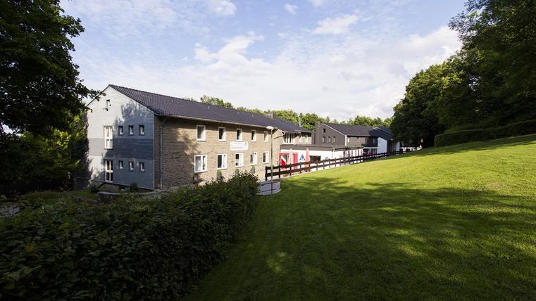 Ein modernes Gebäude inmitten einer grünen Landschaft. Der Himmel ist blau und die Umgebung ist ruhig und einladend.