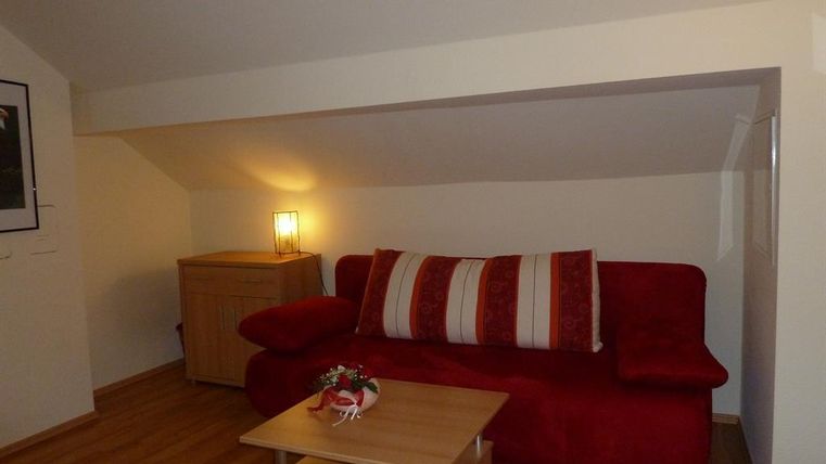 Ein gemütliches Wohnzimmer mit einem roten Sofa und einem kleinen Holztisch. Die Wände sind hell und es gibt eine Lampe, die den Raum behaglich beleuchtet.