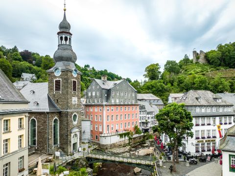 Blick auf die Altstadt von Monschau mit dem markanten Roten Haus und einer Kirche im Vordergrund.