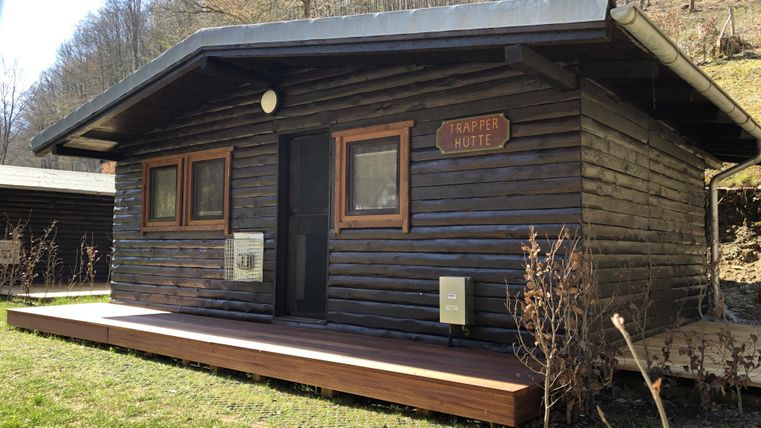 Ein gemütliches Holzhaus mit einem kleinen Veranda. Umgeben von Bäumen und Gras.