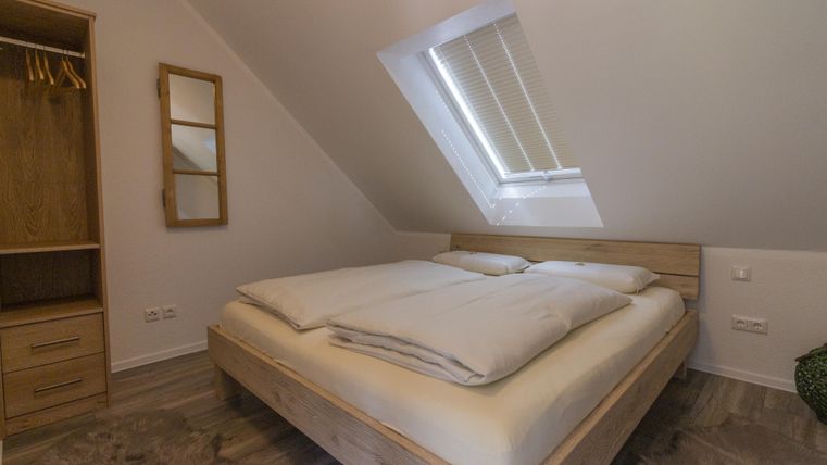 Ein gemütliches Schlafzimmer mit einem großen Doppelbett und Holzmöbeln. Ein Dachfenster sorgt für viel Tageslicht.