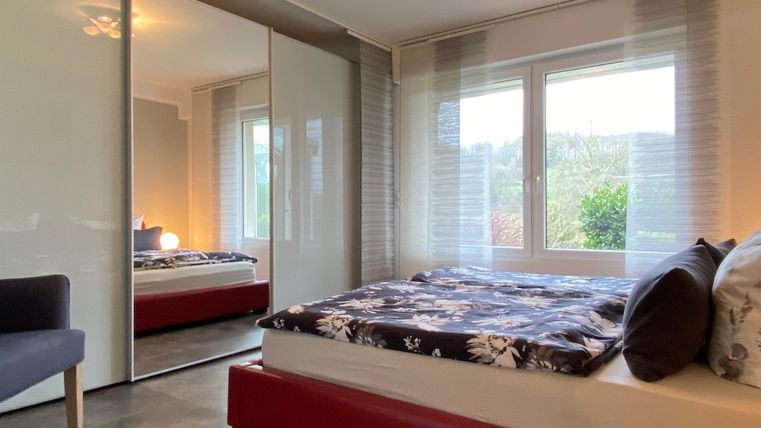 Ein gemütliches Schlafzimmer mit einem großen Bett und einem Spiegel. Die Fenster bieten einen Blick ins Freie und lassen viel Tageslicht herein.