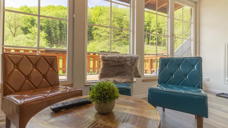 Gemütlicher Wohnbereich mit zwei modernen Stühlen und einem runden Holztisch. Große Fenster bieten einen Blick auf die grüne Landschaft draußen.