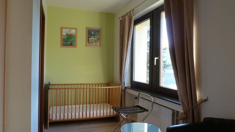 Ein kinderfreundliches Zimmer mit einem Gitterbett und einem kleinen Tisch. Die Wände sind in sanften Farben gestrichen und es gibt große Fenster, die viel Licht hereinlassen.