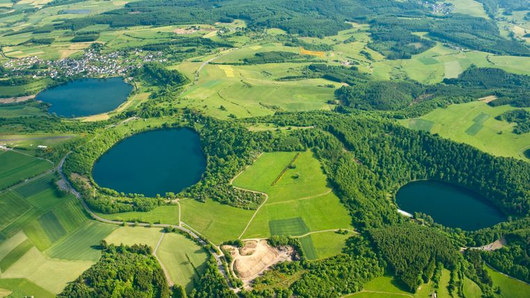 Luftaufnahme der Dauner Maare in der Eifel, umgeben von grünen Feldern und Wäldern.