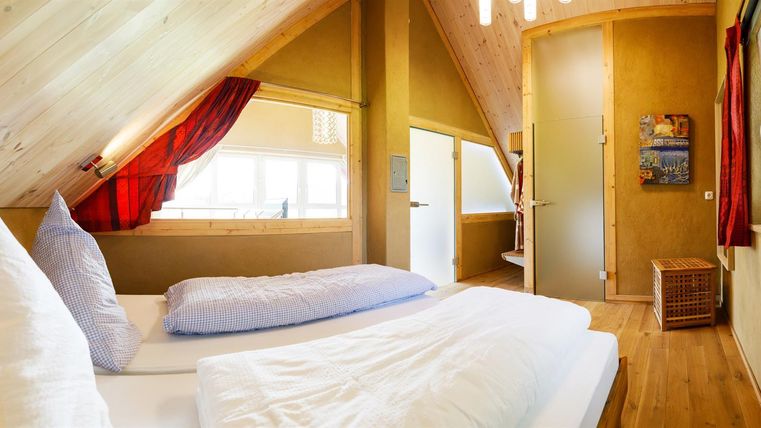 Ein gemütliches Schlafzimmer im Dachgeschoss mit Holzverkleidung und zwei Betten. Helle Fenster sorgen für viel Tageslicht und eine einladende Atmosphäre.