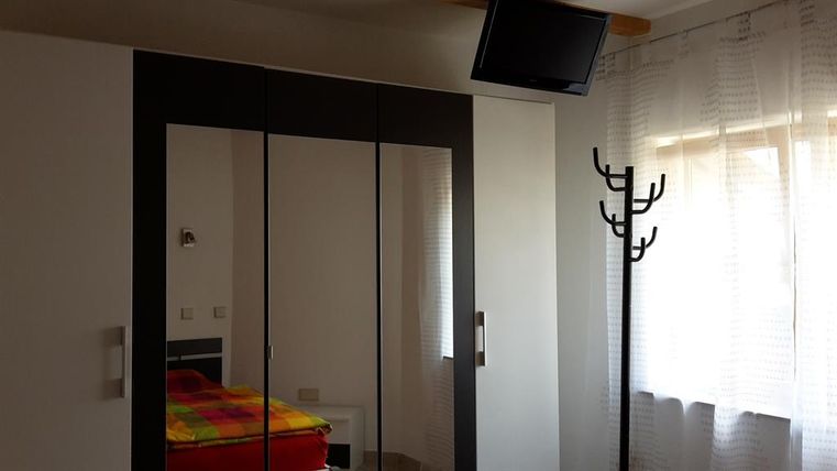 Ein Schlafzimmer mit einem großen Spiegelkleiderschrank und einem Fernseher an der Wand. Der Raum hat ein Bett mit bunter Bettwäsche und einen Garderobenständer.