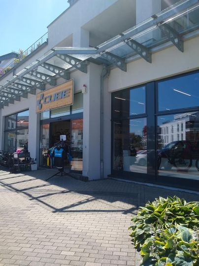 Ein modernes Geschäft mit großen Fenstern und einem einladenden Eingangsbereich. Draußen stehen einige Kunden und Fahrräder.