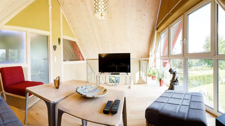 Ein modernes Wohnzimmer mit großen Fenstern und natürlichem Licht. Es gibt gemütliche Möbel und einen Fernseher in einem stilvollen Ambiente.