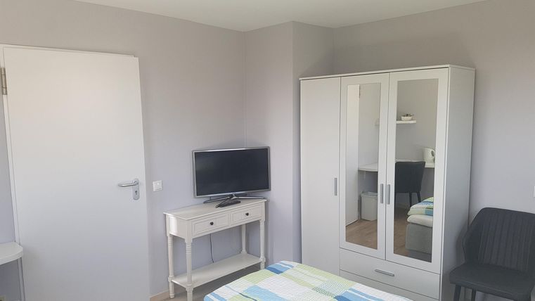 Ein heller, gemütlicher Raum mit einem Doppelbett und einem Fernseher. Der Raum verfügt über einen Kleiderschrank und einen kleinen Tisch.