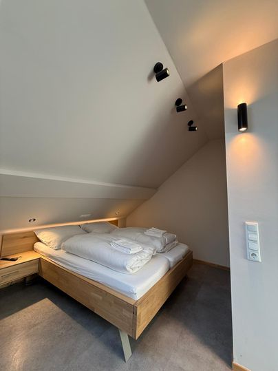 Ein modernes Schlafzimmer mit einem Holzbett und frischer Bettwäsche. Die Wände sind hell, und die Beleuchtung ist warm und einladend.