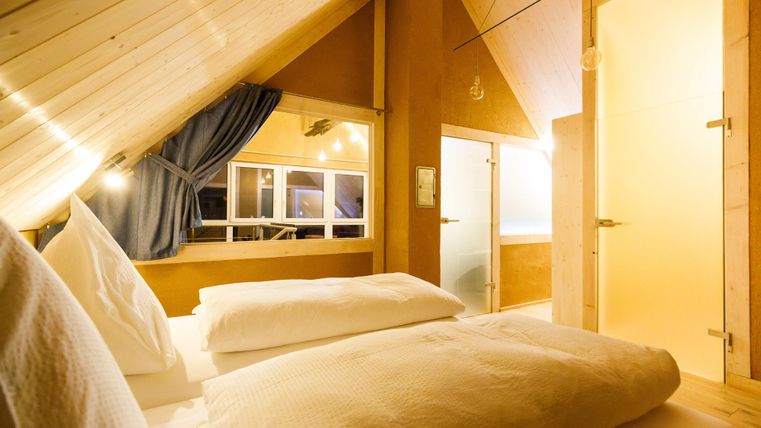 Ein gemütliches Schlafzimmer mit Dachschrägen und Holzverkleidung. Das Zimmer ist hell und einladend, mit einem Fenster und zwei weißen Kissen.