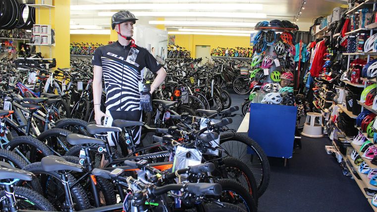 Ein Fahrradgeschäft mit vielen Fahrrädern und Zubehör. Ein Mitarbeiter steht inmitten der Auswahl und trägt einen Helm.