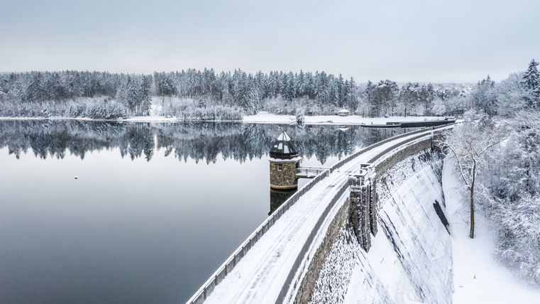 Winterliche Dreilägerbachtalsperre mit verschneiter Landschaft und ruhigem Wasser.