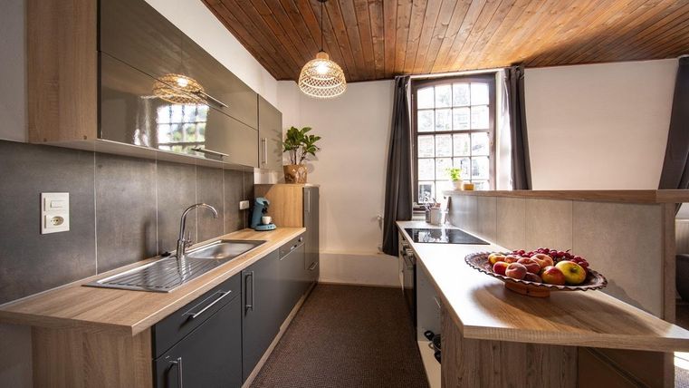 Eine moderne Küche mit Holzregalen und Edelstahl-Geräten. Ein Obstkorb mit Äpfeln und Trauben steht auf der zentralen Insel.