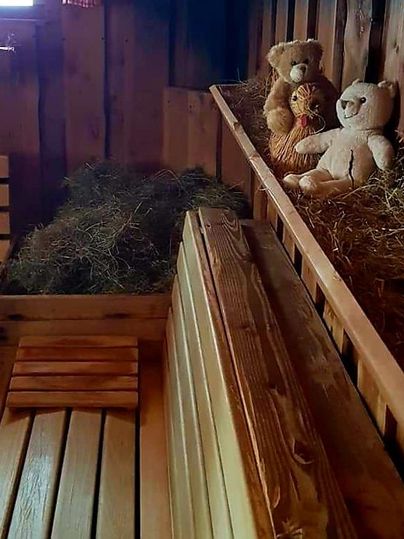 Ein gemütlicher Raum mit Holzverkleidung, in dem zwei Stoffbären neben Heu auf einer Holzablage sitzen. Die Atmosphäre wirkt warm und einladend.