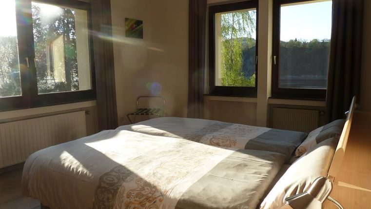 Ein helles Schlafzimmer mit einem großen Doppelbett und großen Fenstern. Das Licht fällt sanft auf die Bettwäsche und den Raum.