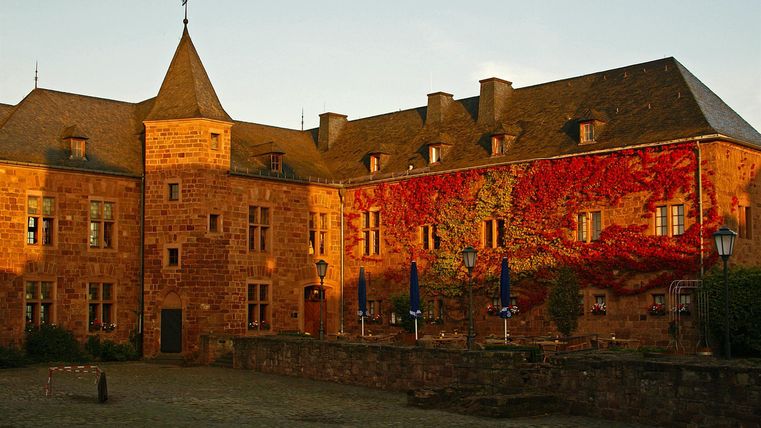 Ein historisches Schloss mit einem charakteristischen Turm und einer bunten Wandmalerei. Das Gebäude ist von sanftem Licht umgeben und strahlt eine einladende Atmosphäre aus.