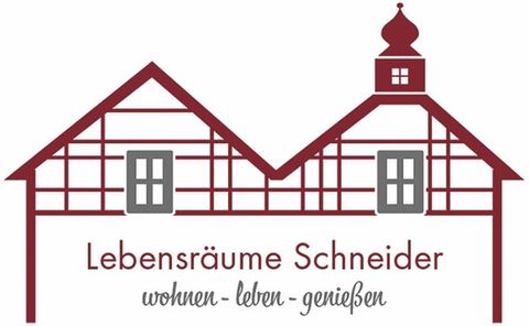 Ein Logo mit zwei stylisierten Häusern im Fachwerkstil. Darunter steht "Lebensräume Schneider" mit dem Slogan "wohnen - leben - genießen".