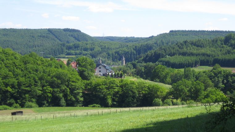 Landschaftsansicht mit grünen Hügeln und einem Dorf in der Ferne.