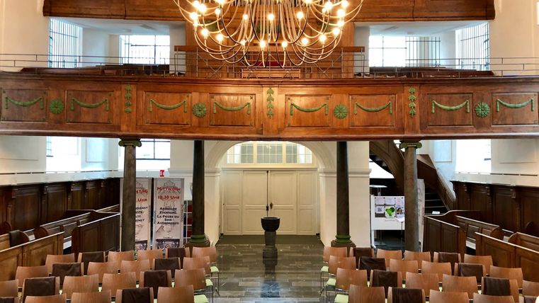 Ein stilvoller Innenraum mit Holzbänken und einem eleganten Kronleuchter. Der Raum ist hell und einladend, ideal für Veranstaltungen.