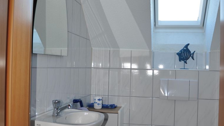 Ein modernes Badezimmer mit weißen Fliesen und einem kleinen Fenster. Es gibt ein Waschbecken und eine Toilette, sowie ein paar dekorative Elemente.