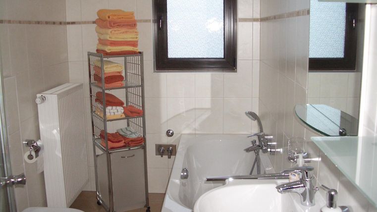 Ein modernes Badezimmer mit einer Badewanne, einem Waschbecken und einem WC. Auf einem Regal sind mehrere Handtücher ordentlich gestapelt.
