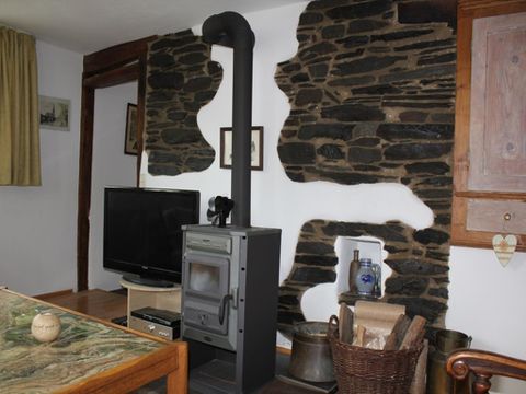 Ein gemütliches Wohnzimmer mit einem Holzofen und einer Steimauer. Im Hintergrund steht ein Fernseher und es gibt rustikale Möbel.